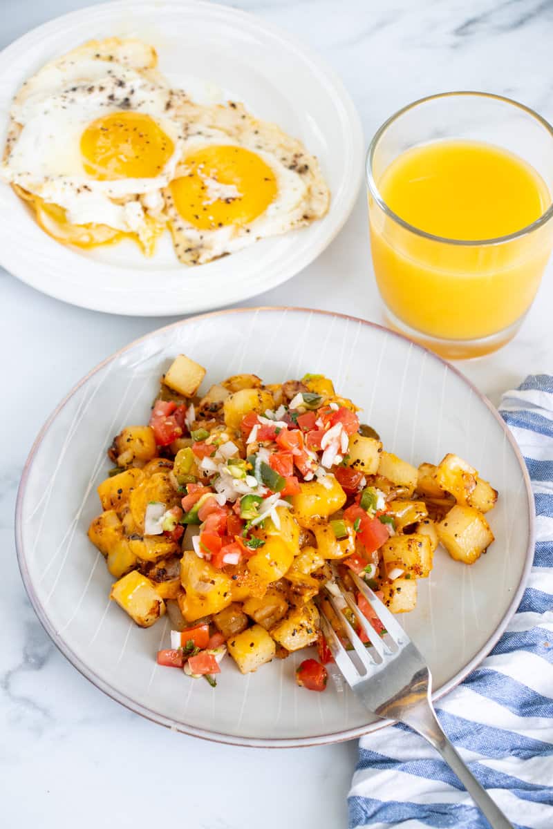 Breakfast potatoes on a plate with eggs and orange juice