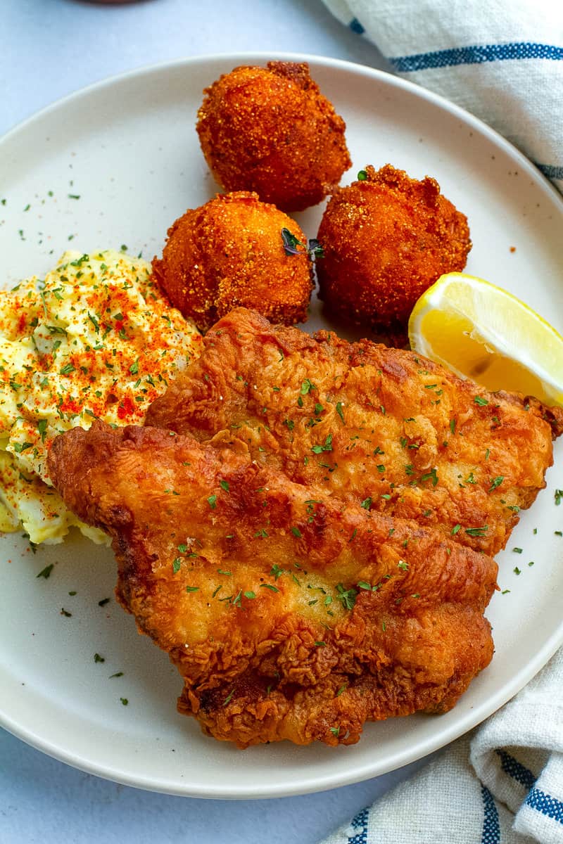 Overhead of southern fried fish on a plate with potato salad and hushpuppies