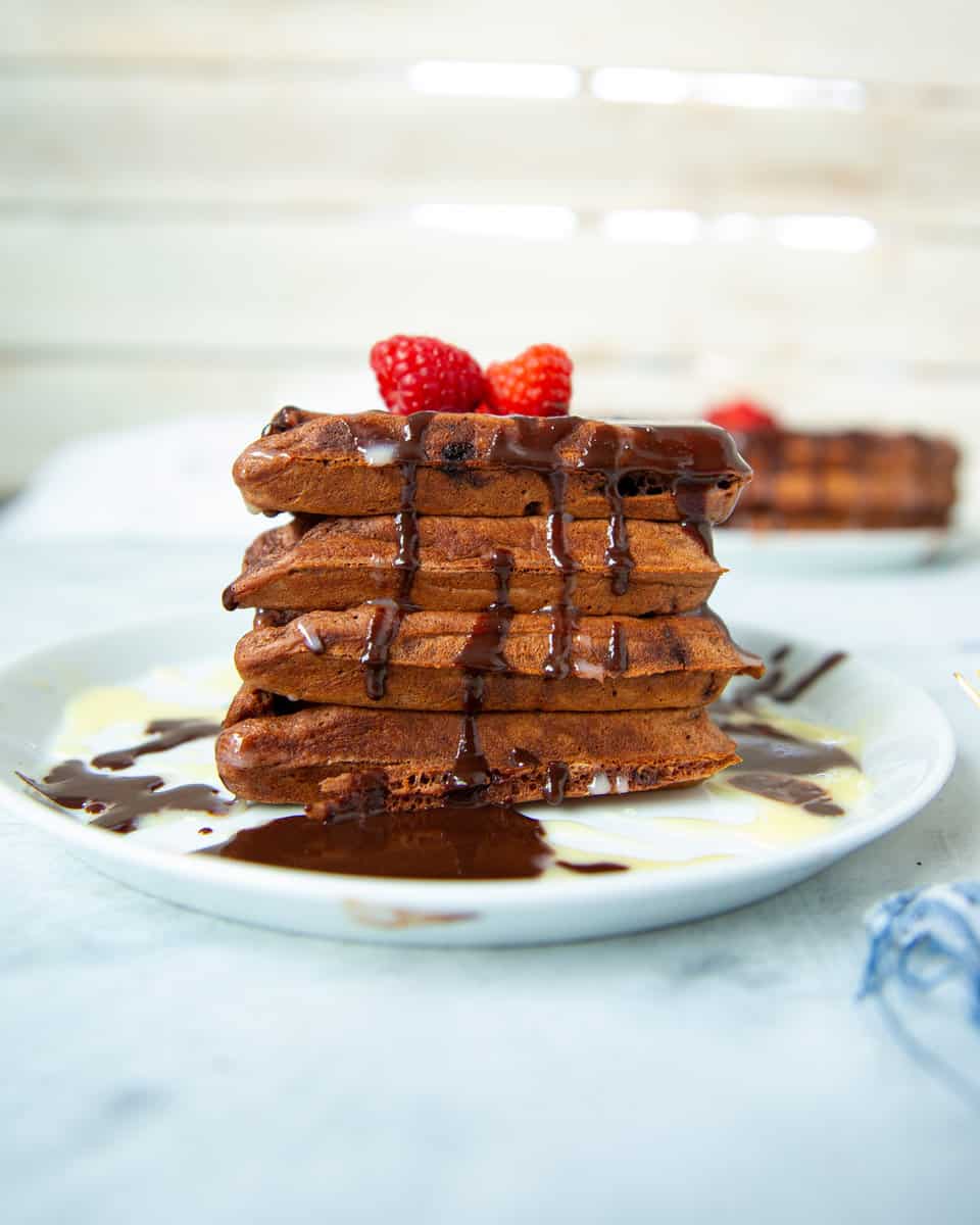 stack of chocolate waffles on a plate with chocolate sauce, white chocolate sauce and raspberries
