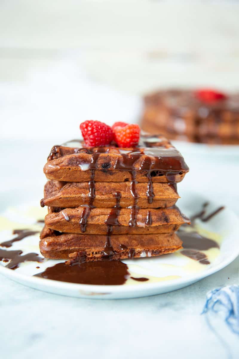 stack of chocolate waffles on a plate with chocolate sauce, white chocolate sauce and raspberries