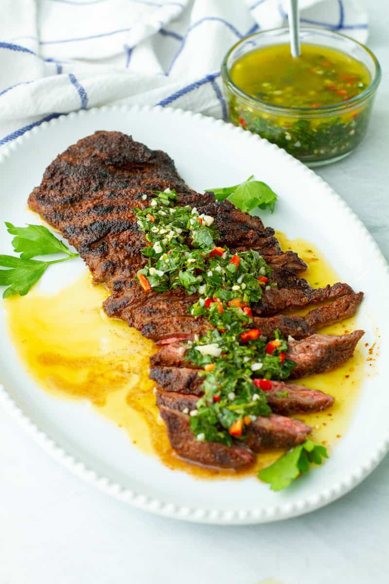 Grilled Skirt Steak Topped with Chimichurri Sauce on a platter.