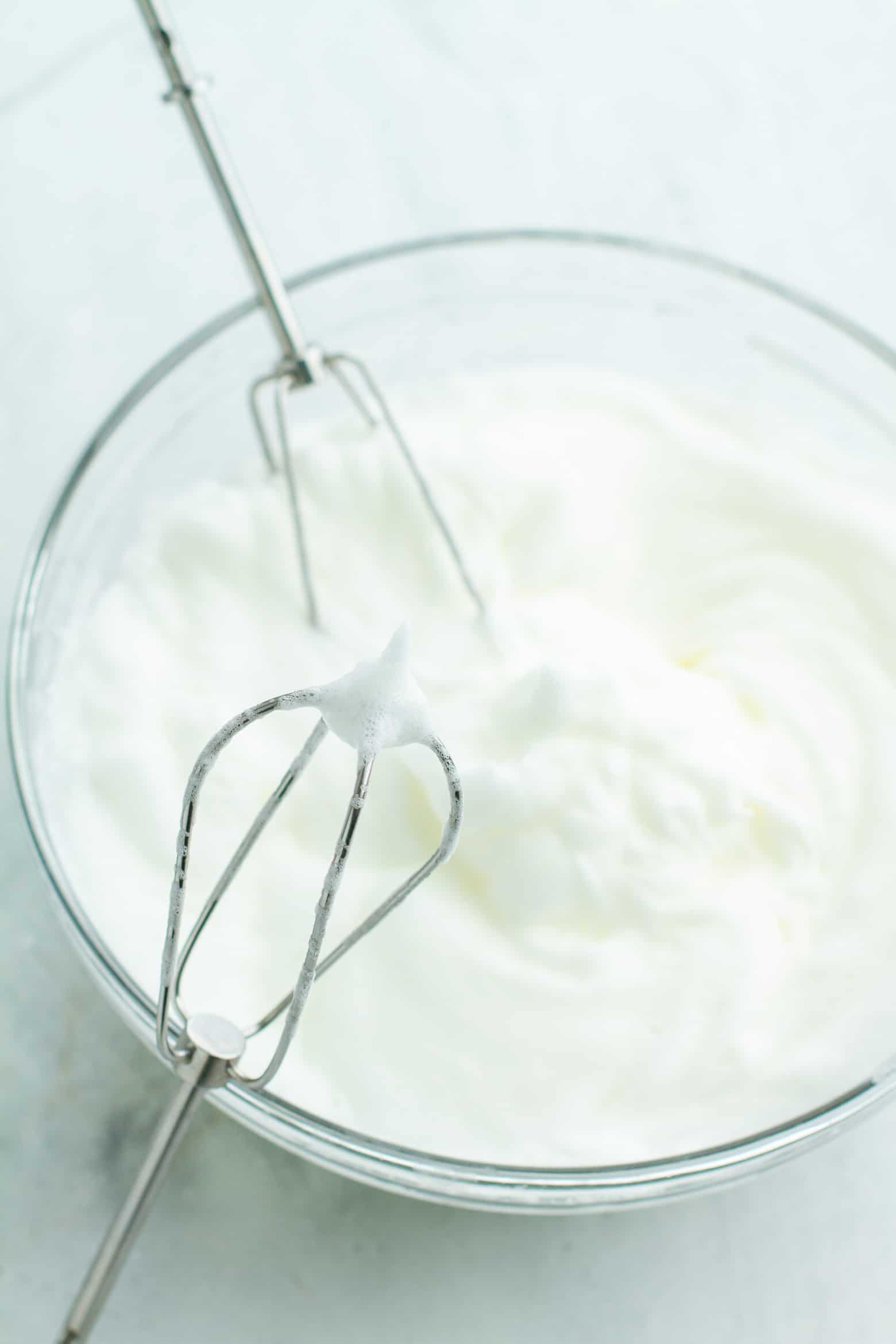 Egg whites beat to a stiff peak in a bowl with beaters.
