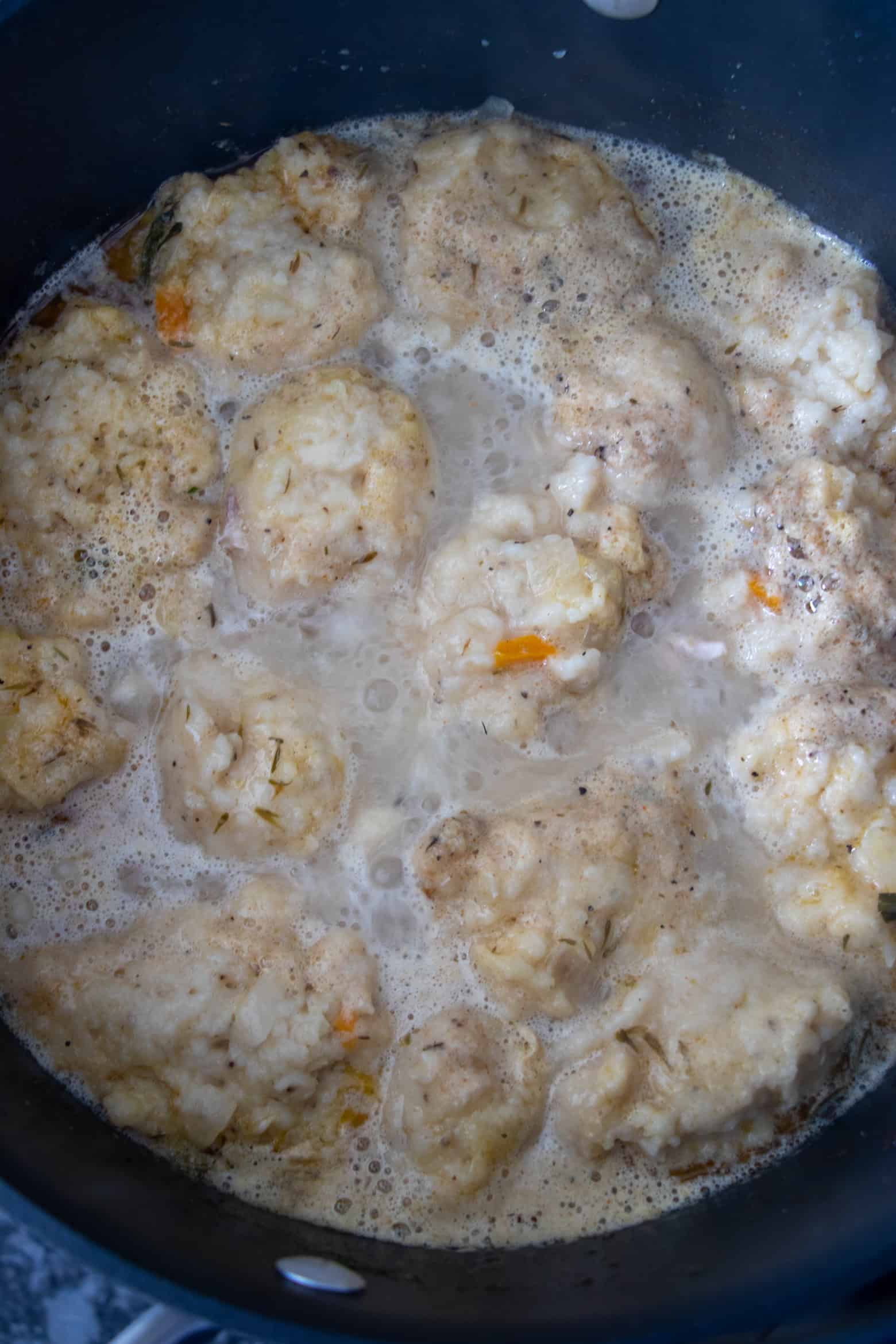 Dumplings cooking in broth in a pot.
