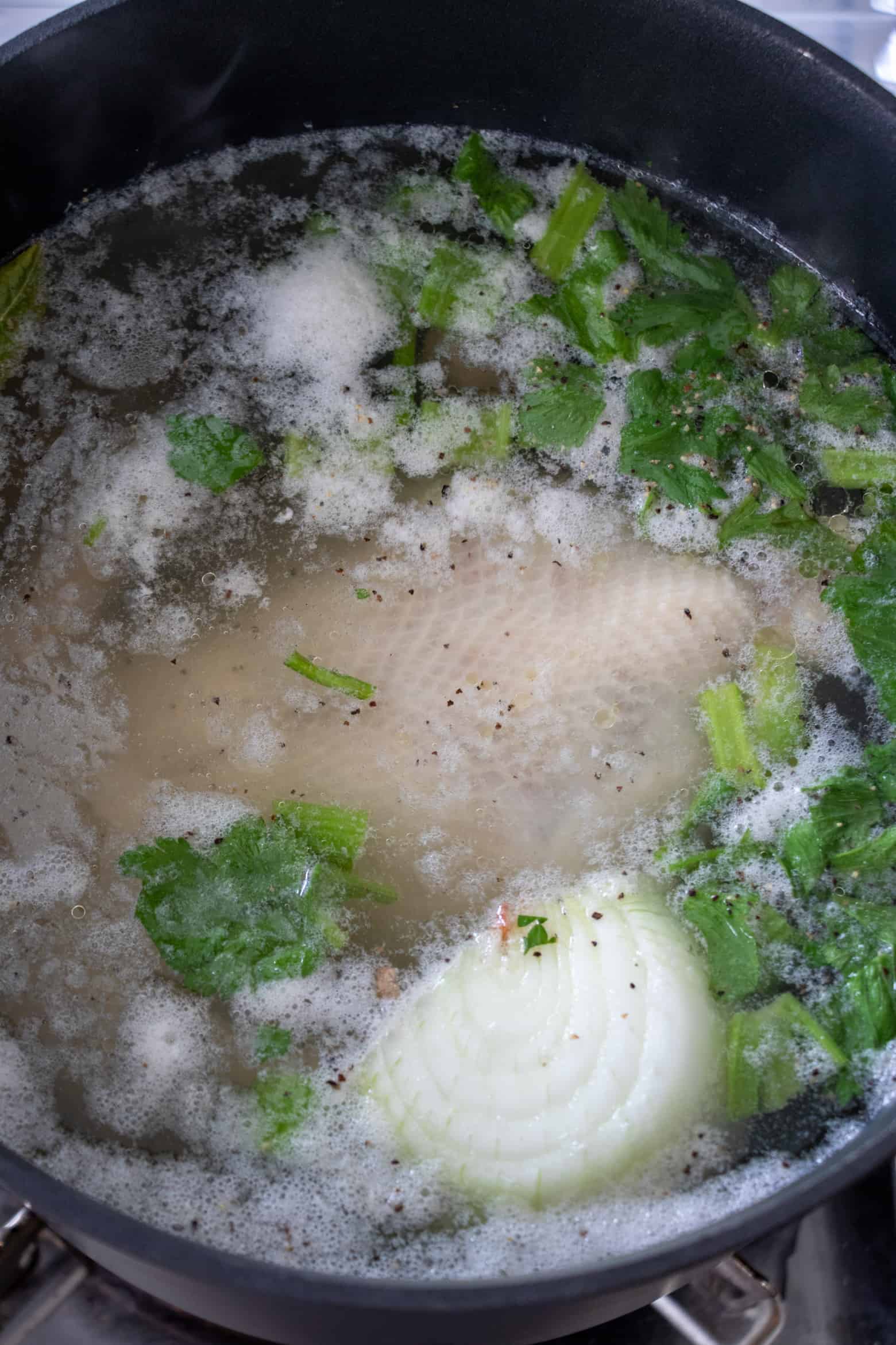 Whole chicken and aromatics in a pot with foam.