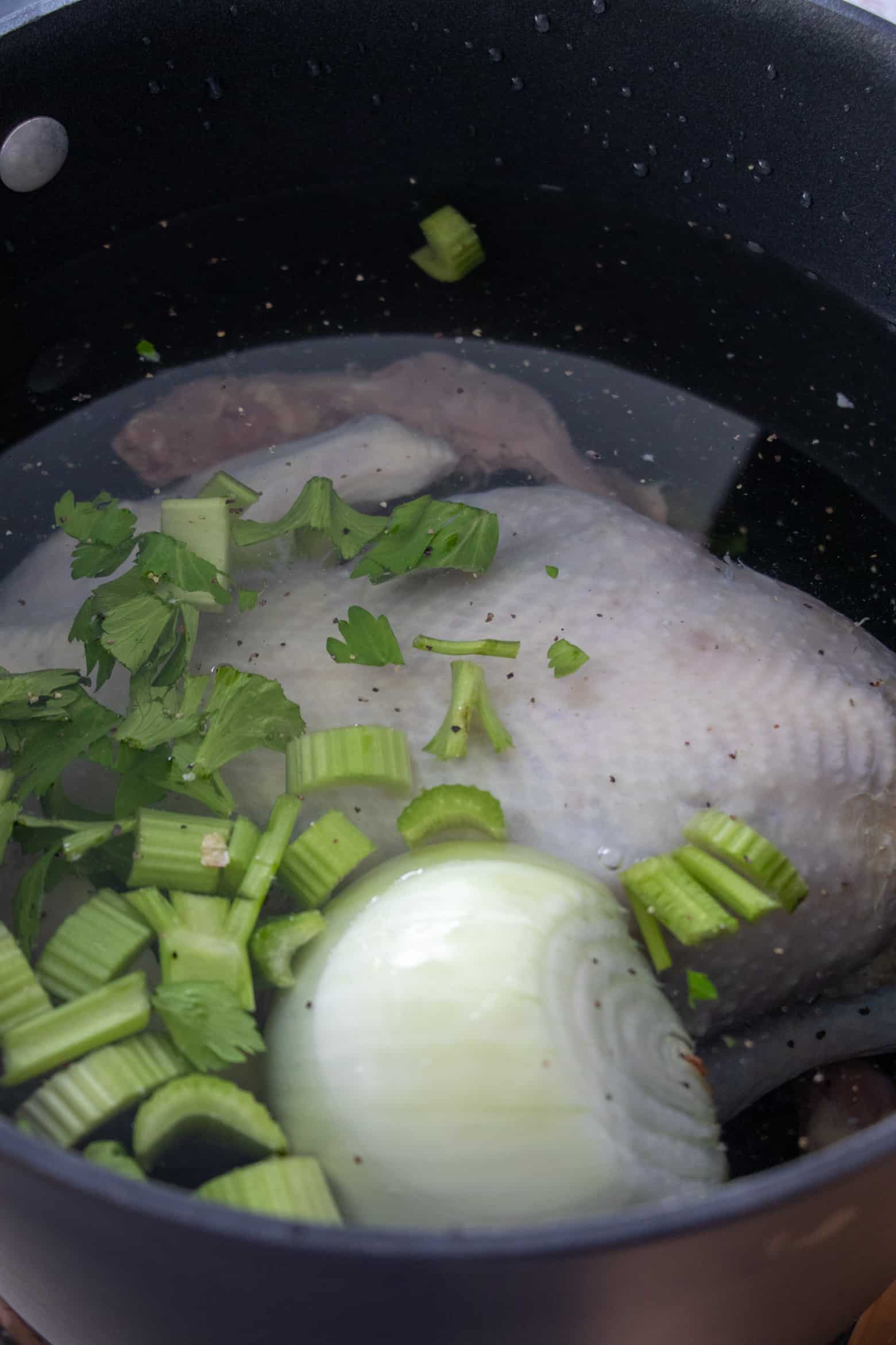 Whole chicken and aromatics in a pot.