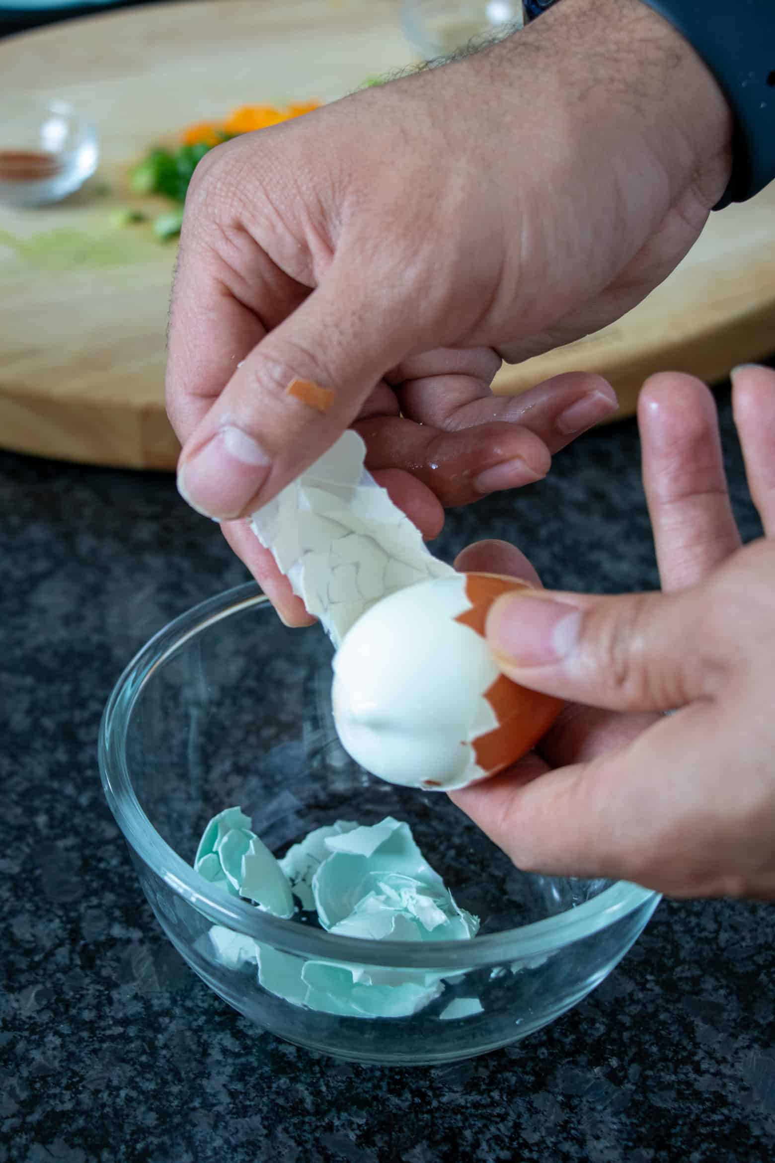 Hard boiled egg being peeled over a bowl.