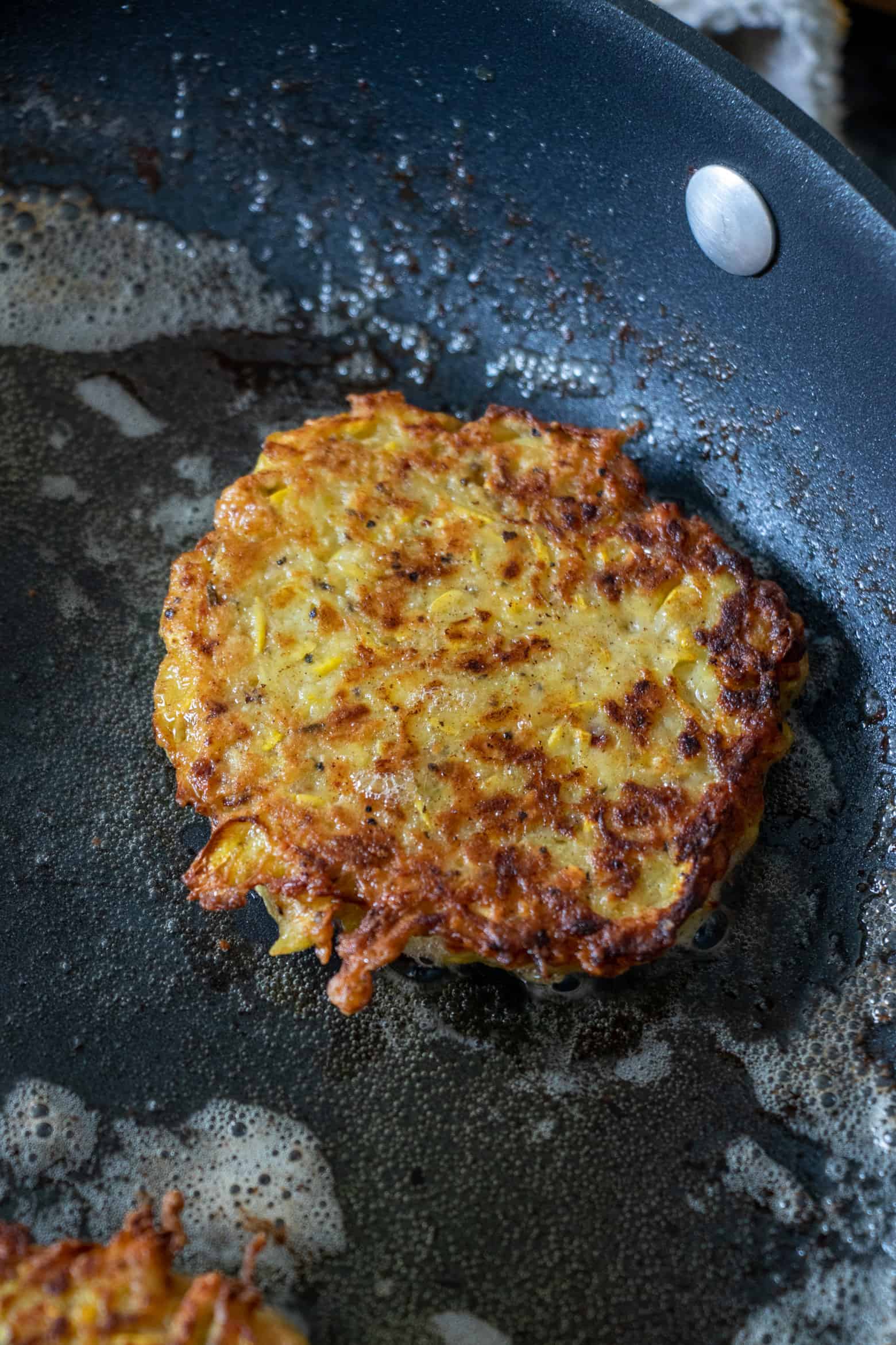 Yellow squash fritter cooking in a skillet