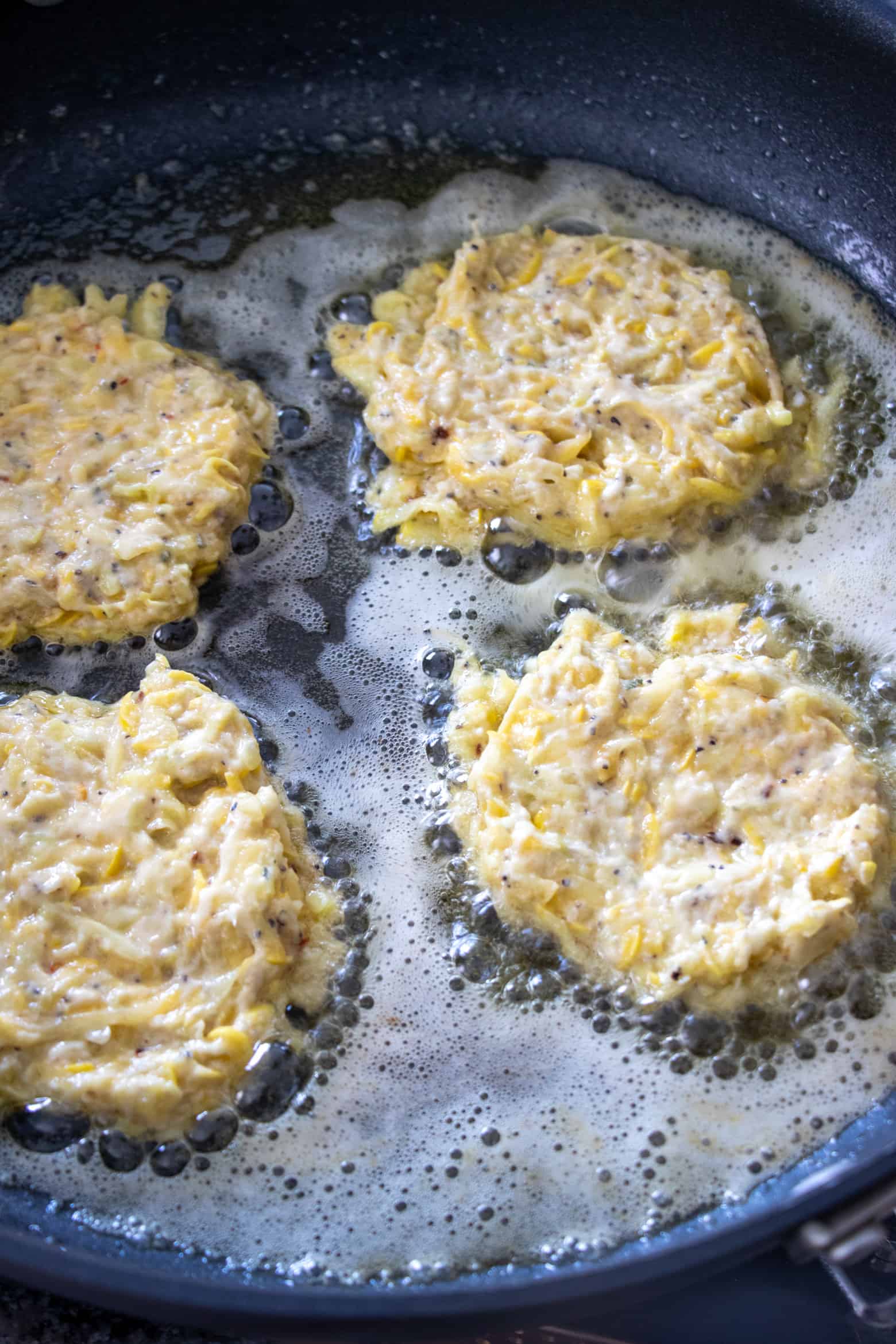 Squash fritters cooking in a skillet.