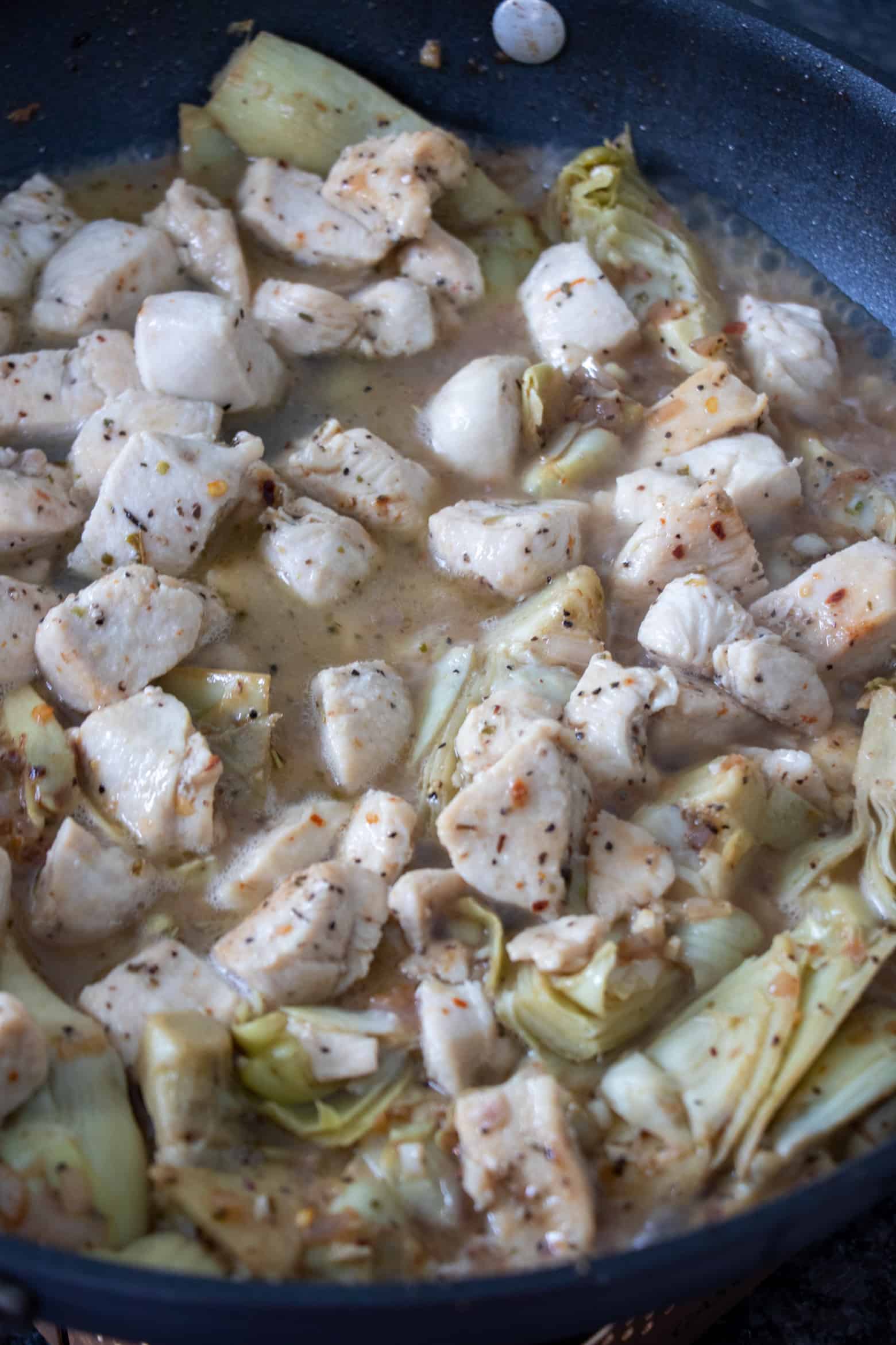 chicken cooking in a pan with white wine and aromatics.