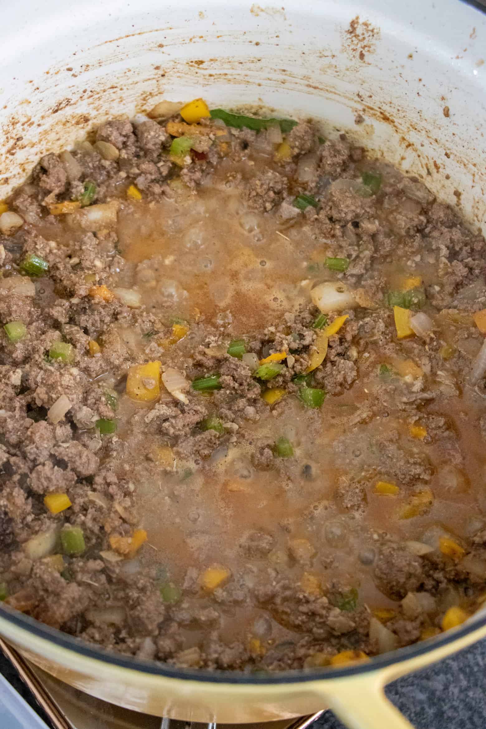 Dirty rice mixture of vegetables, ground beef, and stock cooking in a pot.