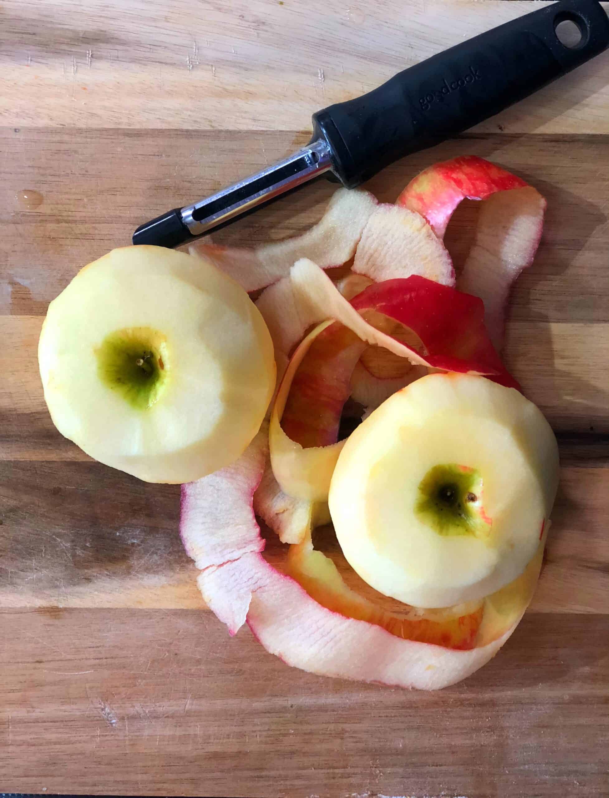 Peeled Apples next to a vegetable peeler.