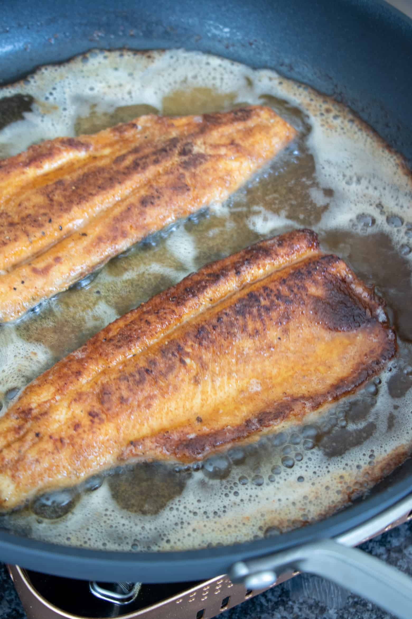 Trout fillets cooking in a skillet.
