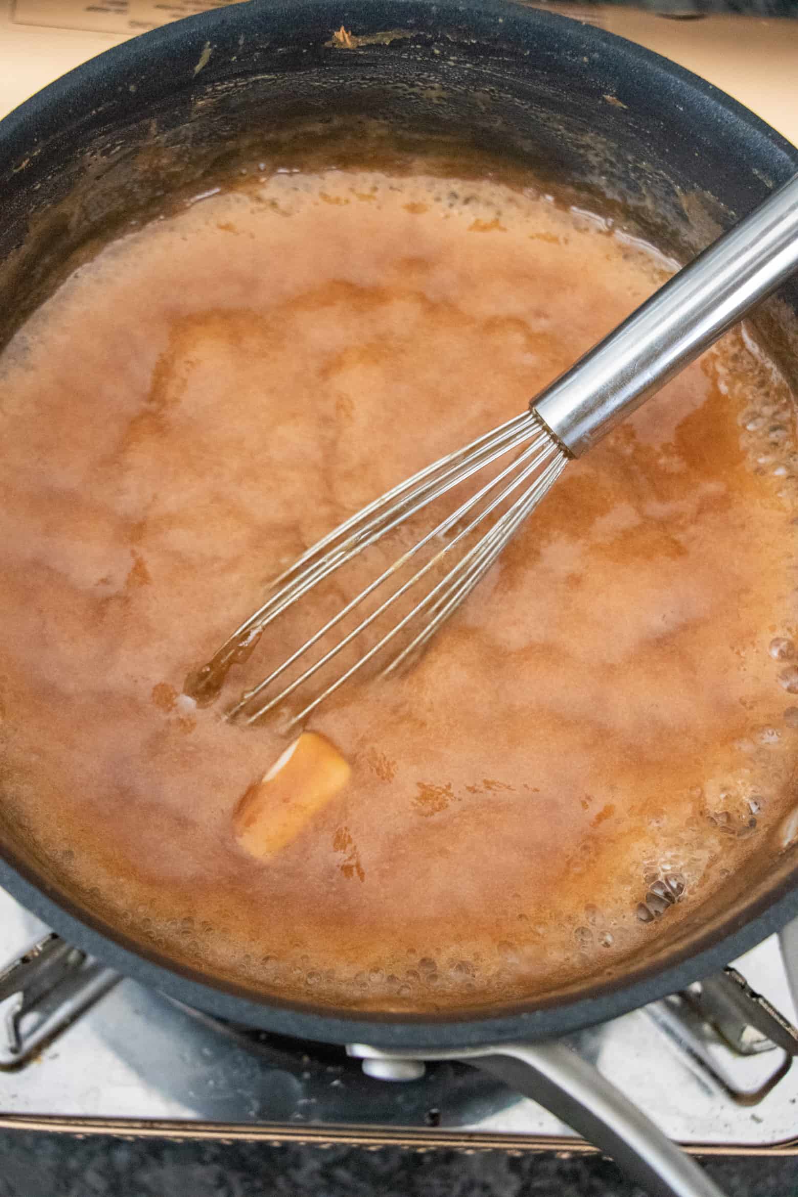 Butter being stirred into caramel sauce in a pot.
