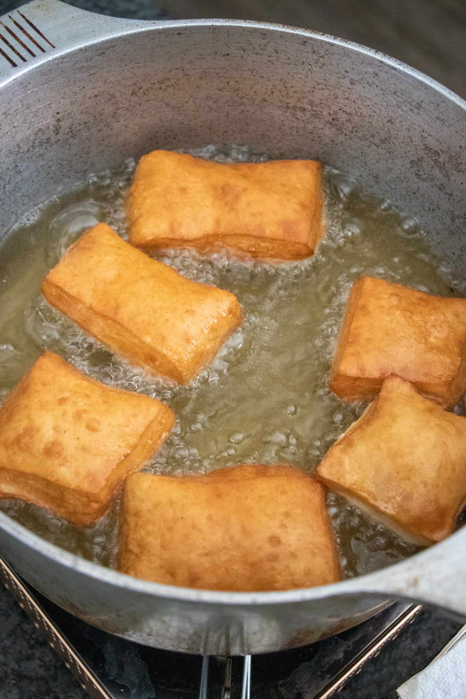 Beignets frying in a pot of oil.