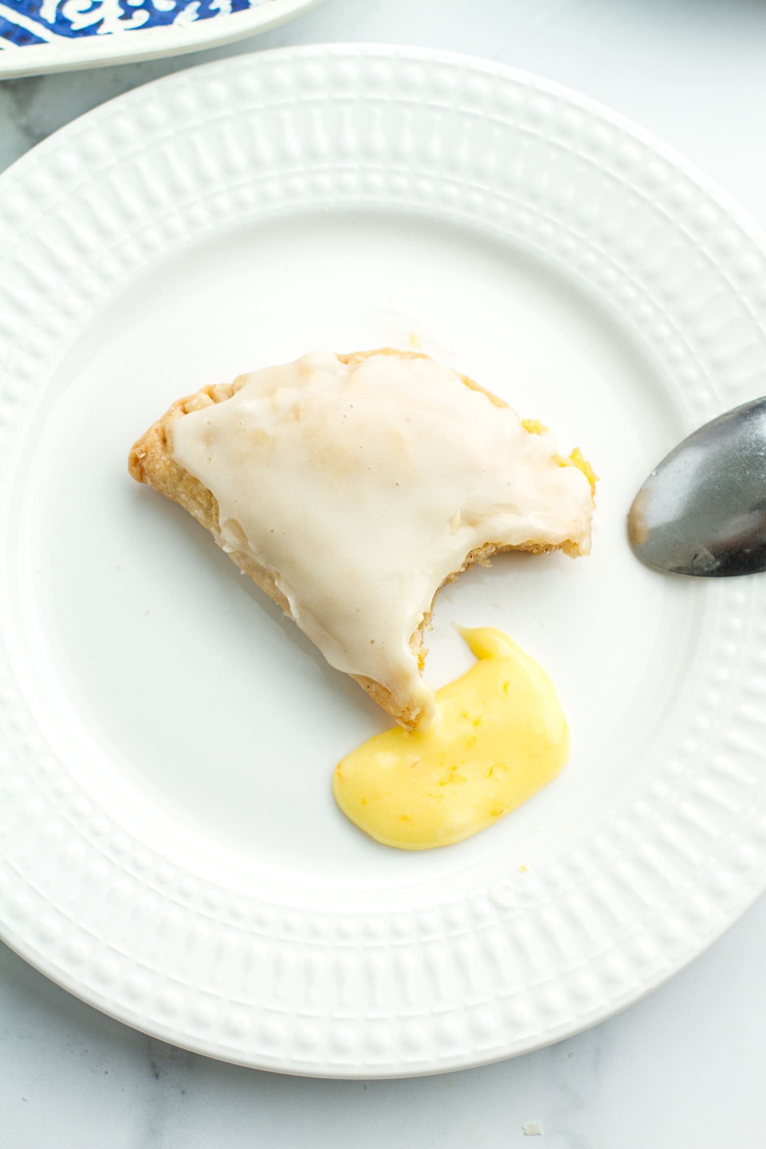 Lemon hand pie on a plate with a bite missing with some lemon curd on the plate.