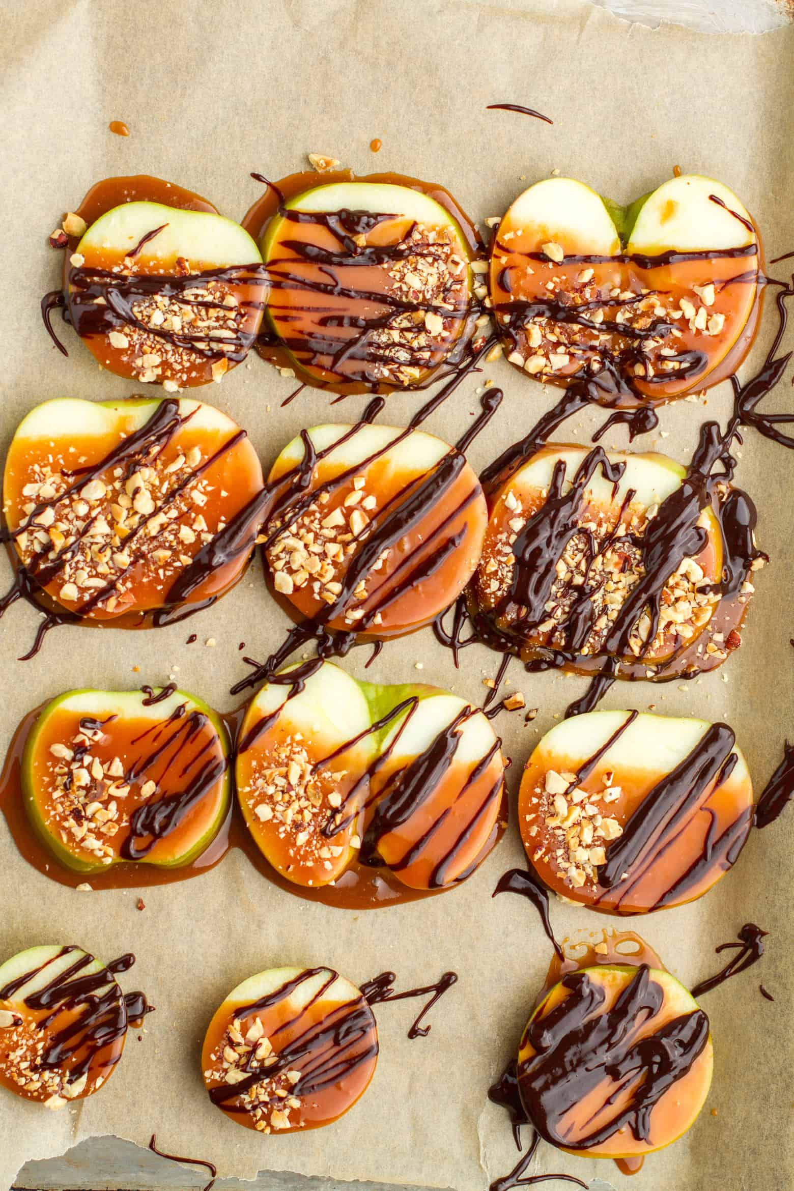 Caramel Apple Slices covered with chocolate sauce and chopped nuts on a baking sheet