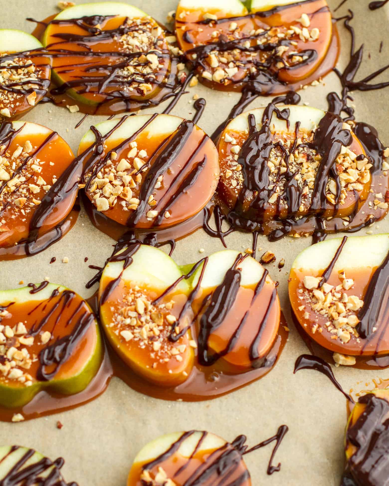 Close up of Caramel Apple Slices covered with chocolate sauce and chopped nuts on a baking sheet