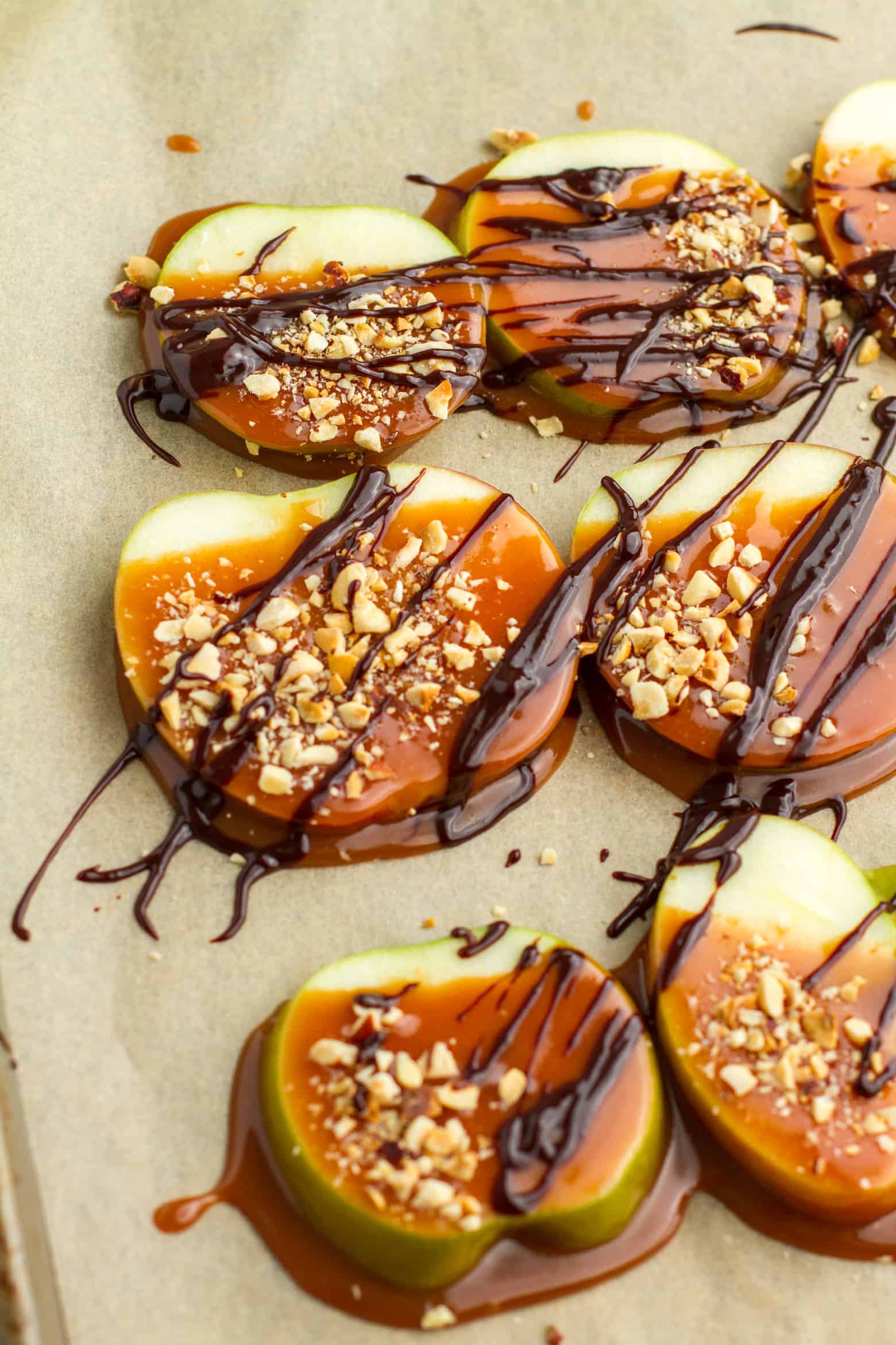 Close up of Caramel Apple Slices covered with chocolate sauce and chopped nuts on a baking sheet