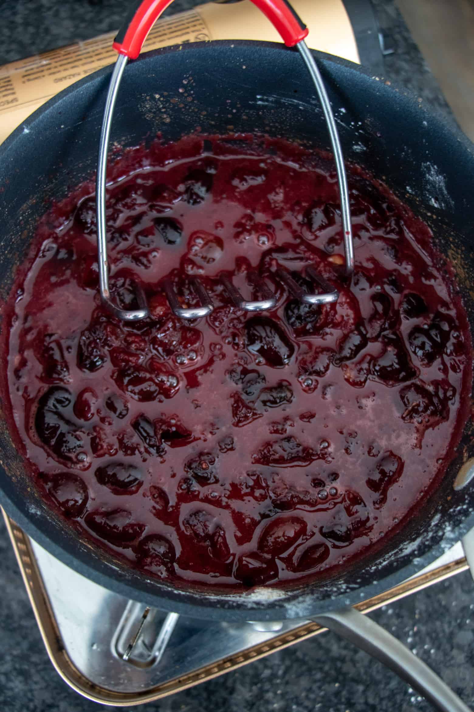 Cherry pie filling ingredients being mashed in a pot.