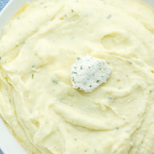 mashed potatoes in a serving dish with a scoop of boursin cheese in center
