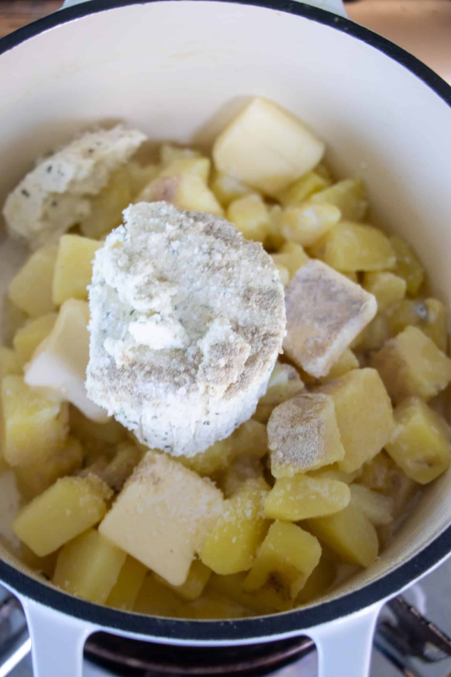 boursin cheese and seasonings being added to potatoes in pot