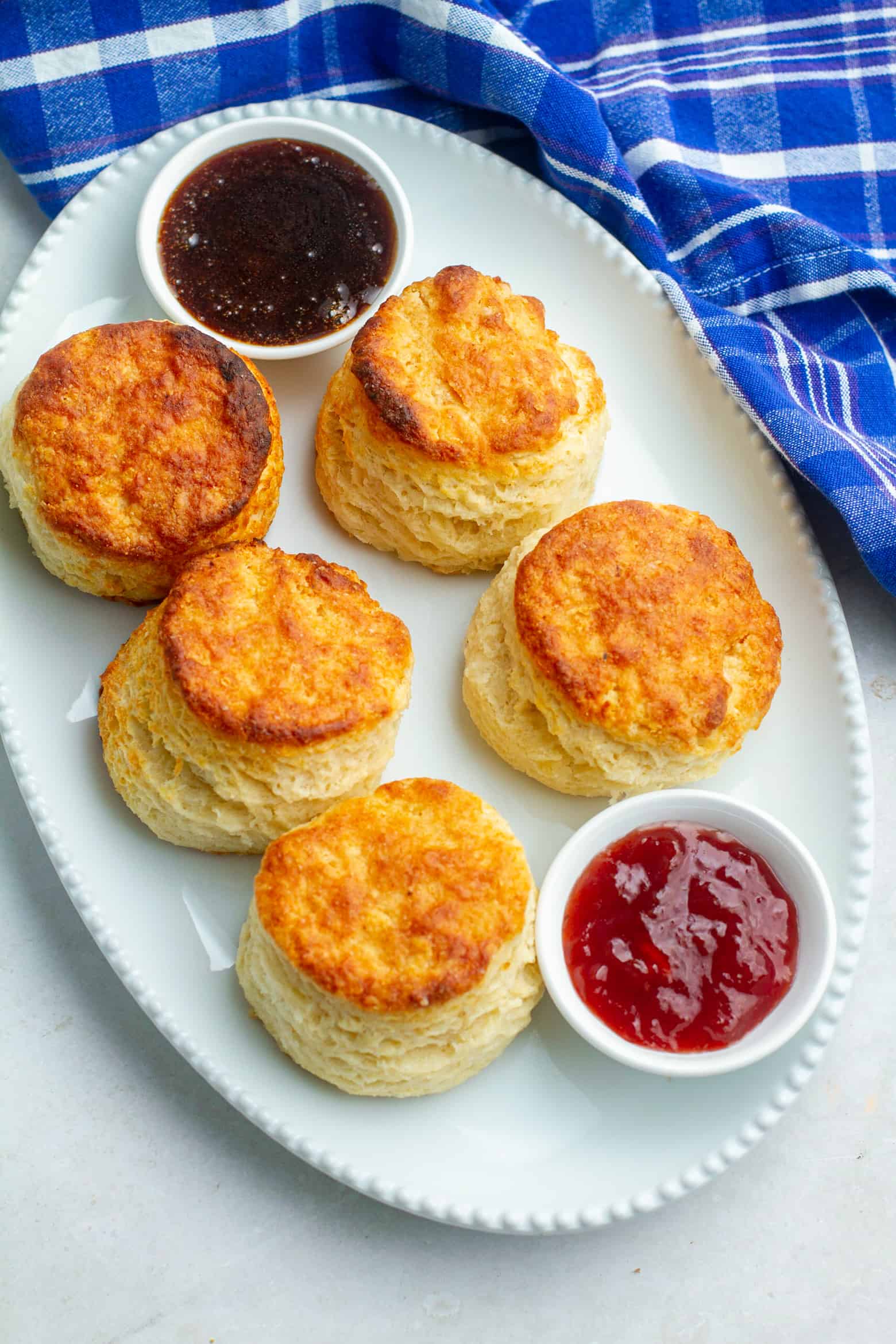 Flaky buttermilk biscuits on a platter with honey and jam.