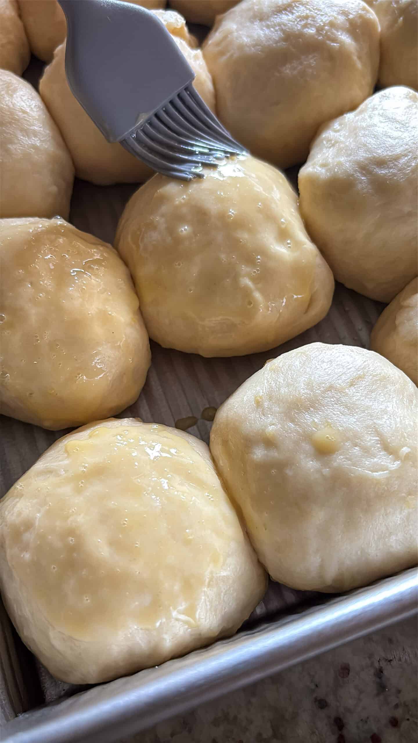 Proofed dough balls being brushed with egg wash.