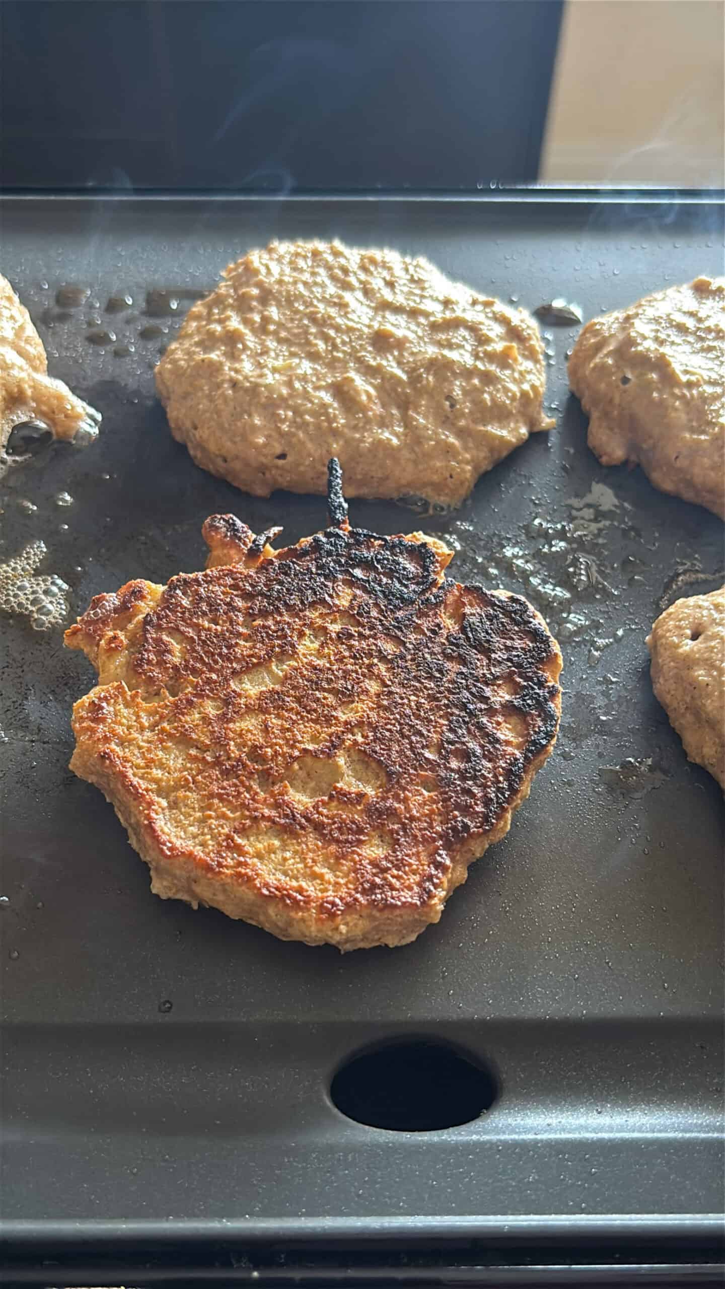 Apple oat pancakes cooking on a griddle.