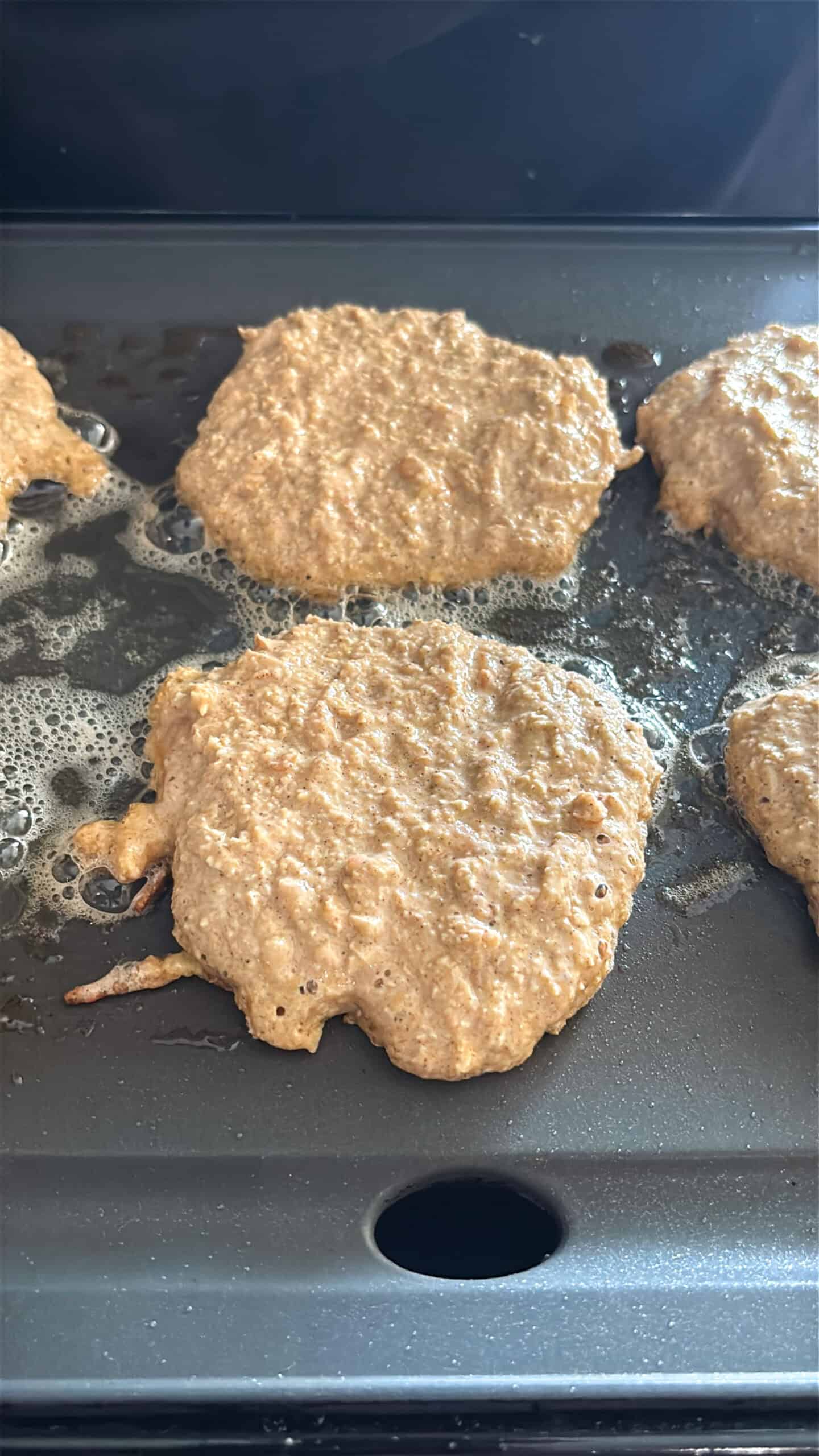 Apple oat pancakes cooking on one side.