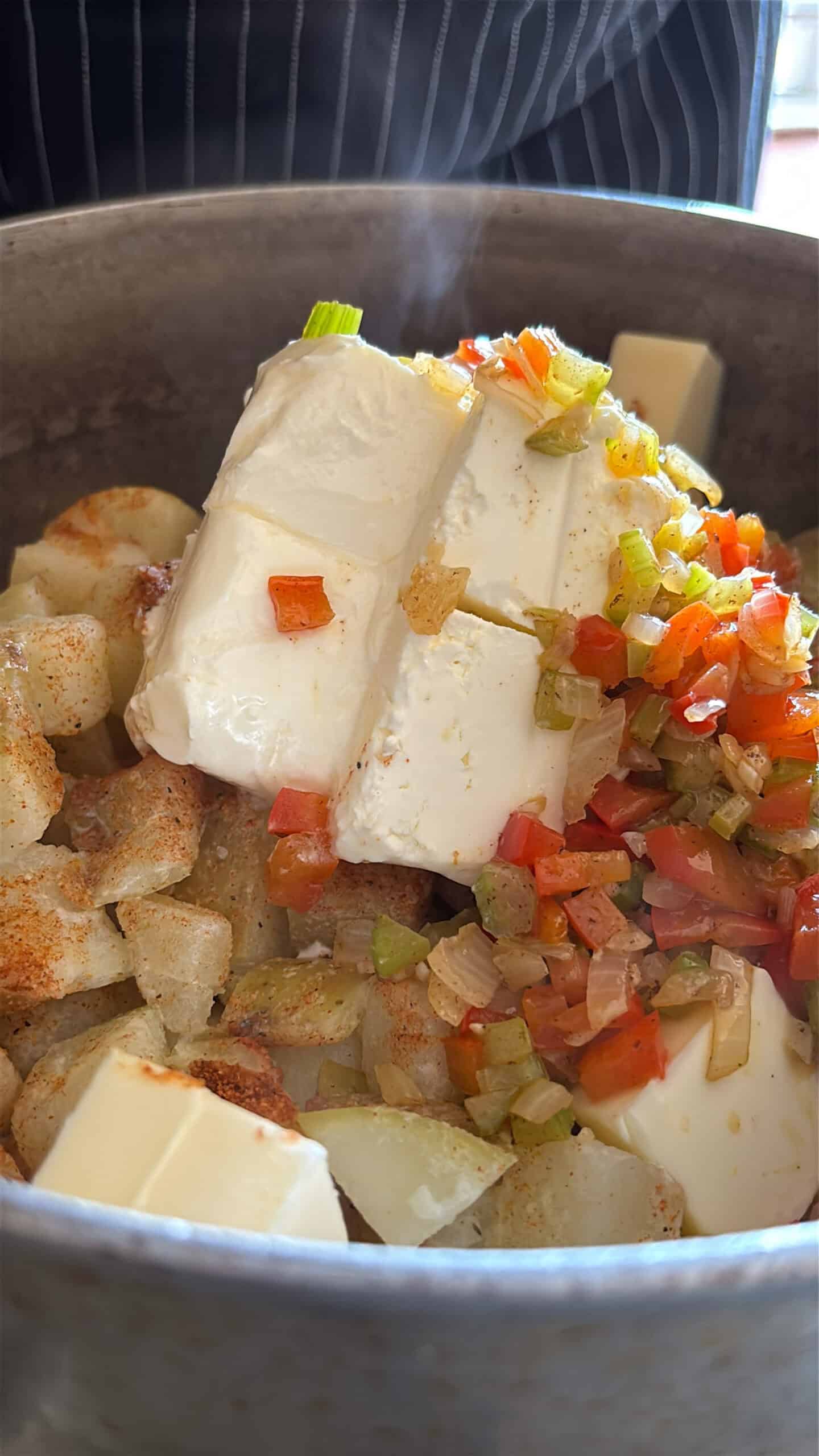 Vegetables and cream cheese being added to cooked potatoes.