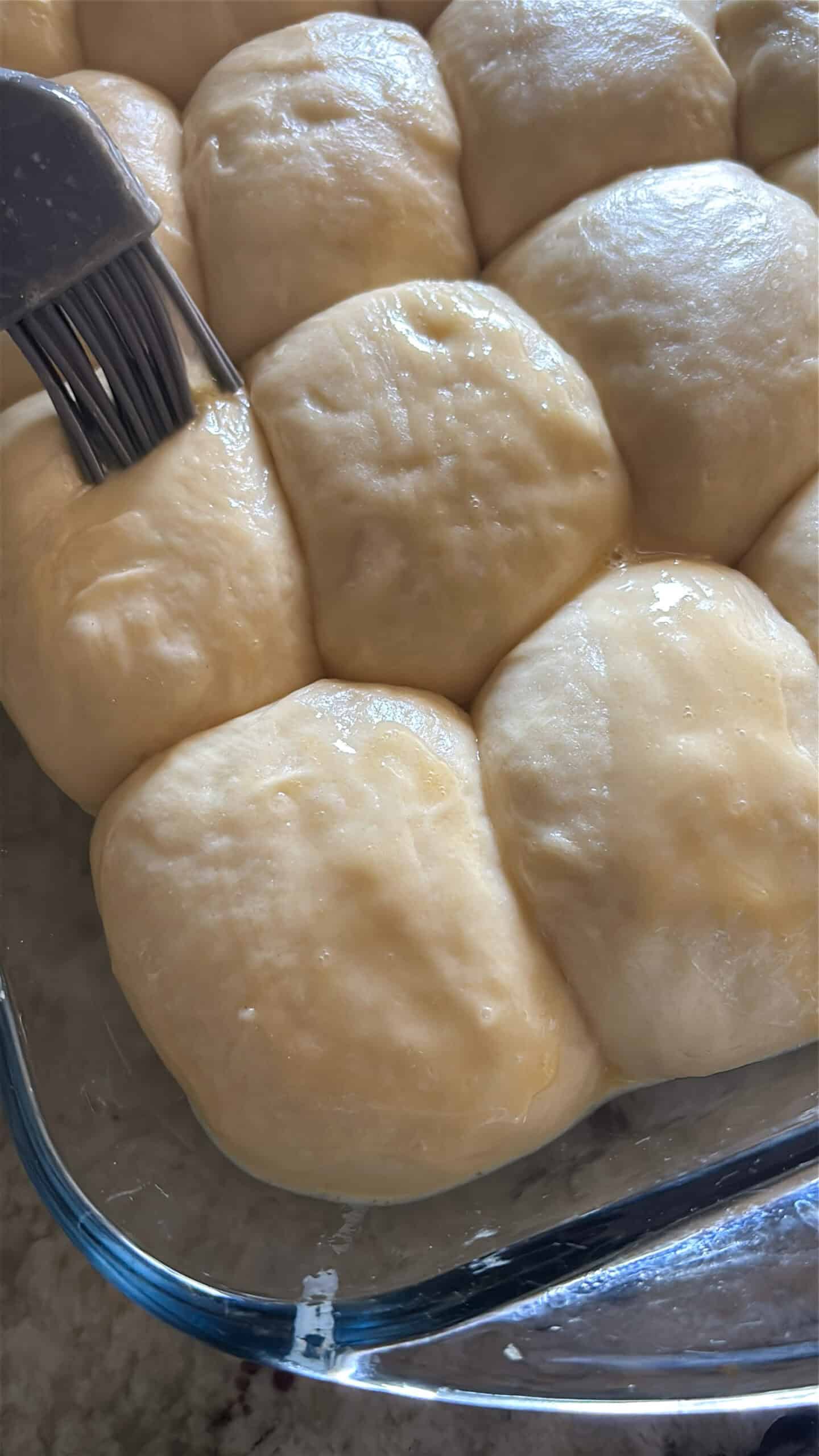 Raw honey butter rolls being brushed with egg wash before baking.