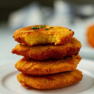 A stack of hot water cornbread with a bite taken out of one.