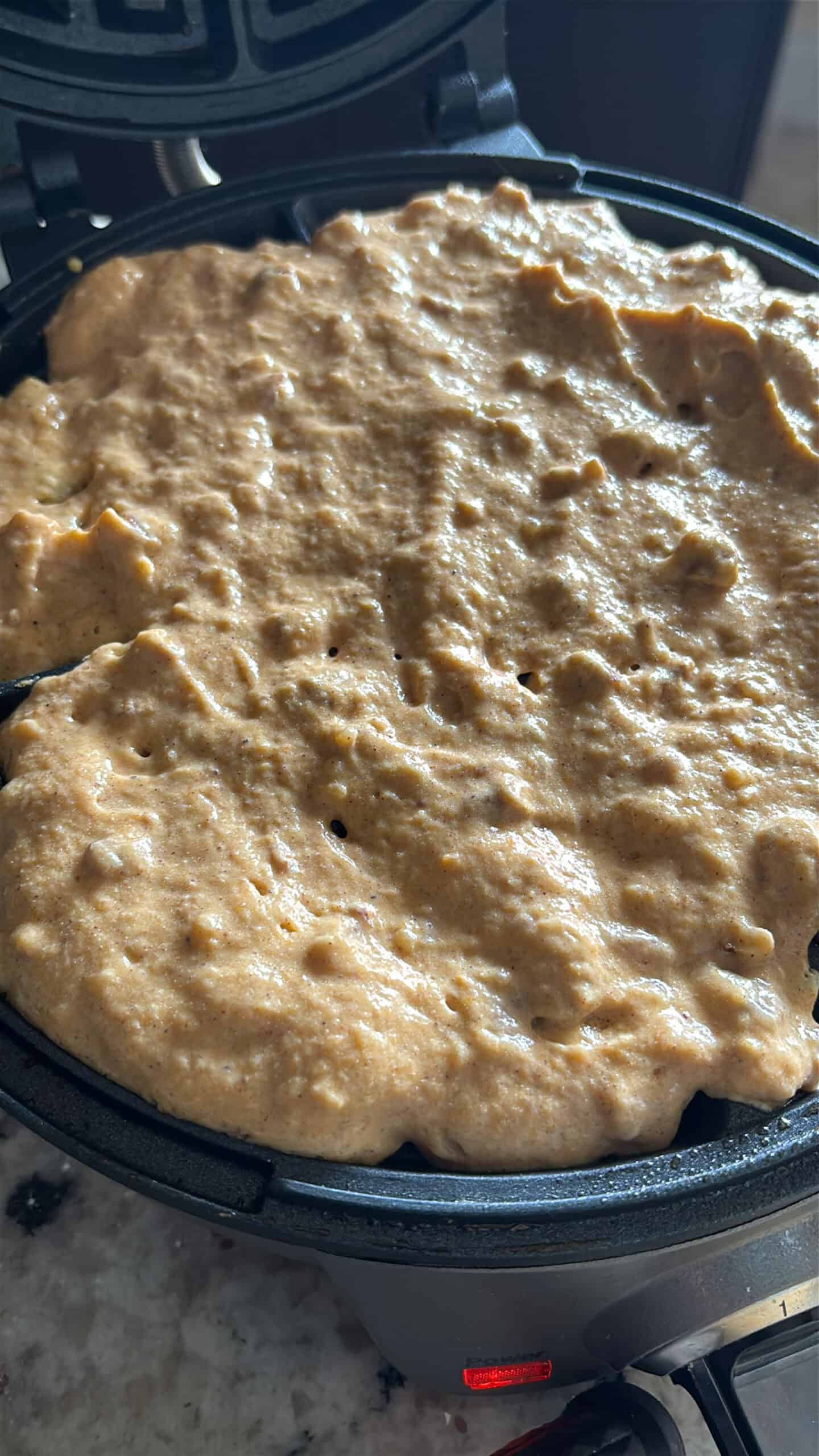 Pumpkin pecan waffles cooking in a waffle iron.