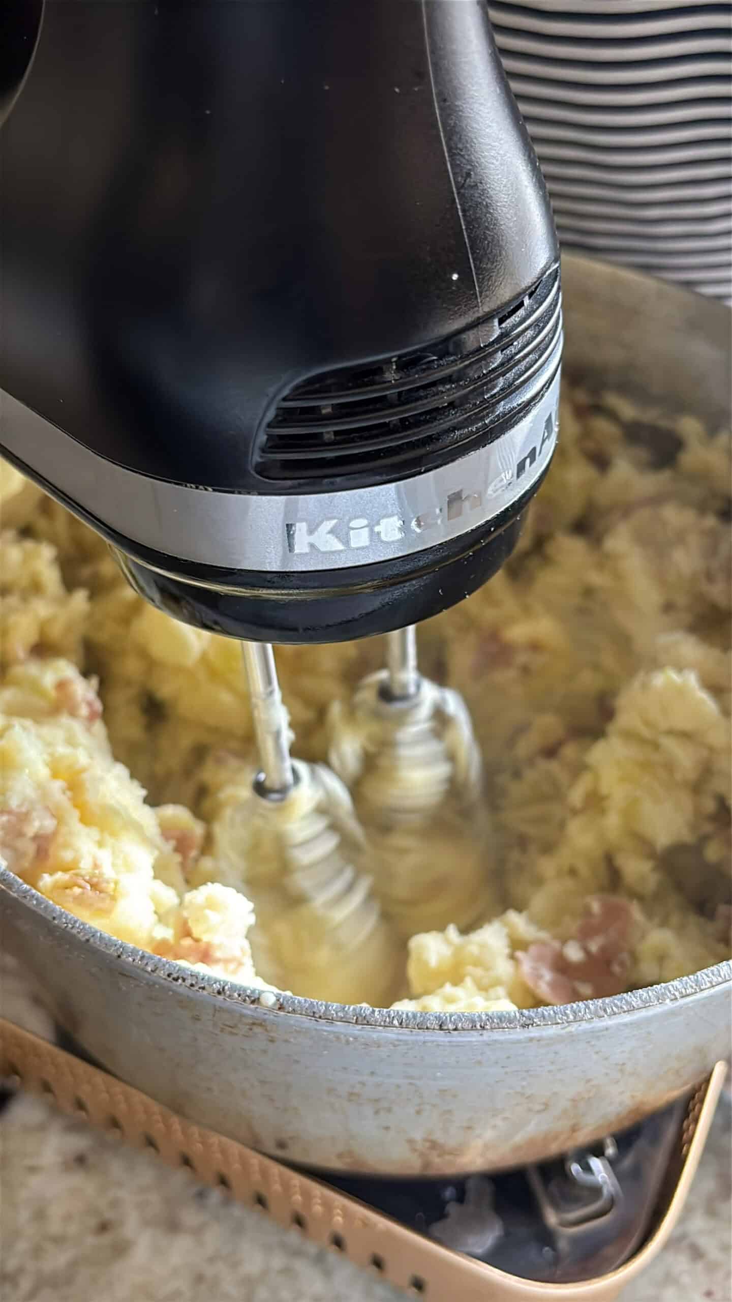 A hand mixer mixing potatoes in pot.