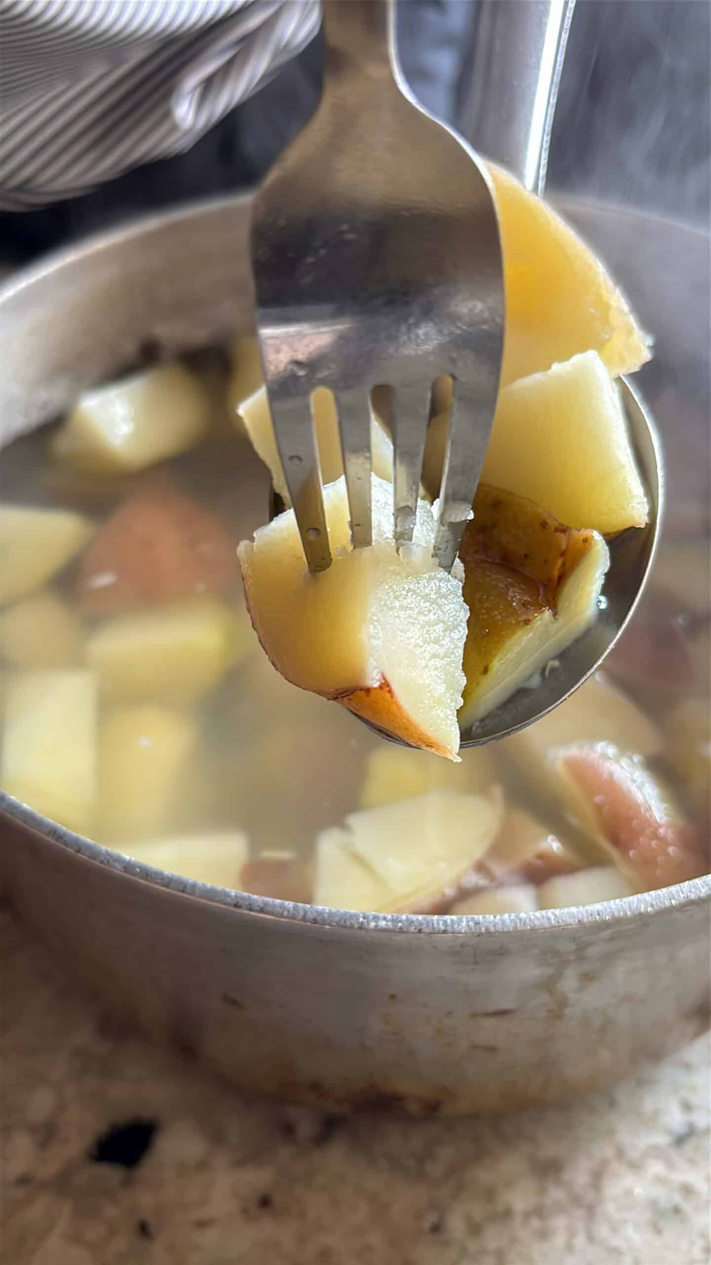 Fork piercing cooked potatoes.