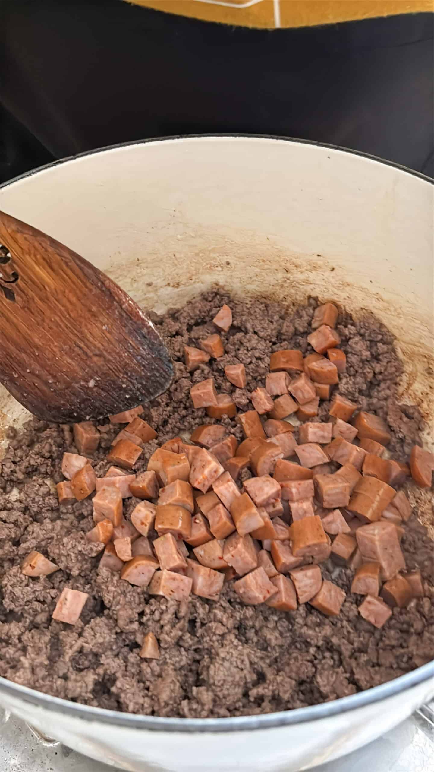 Ground beef and smoked sausage cooking in a Dutch oven.