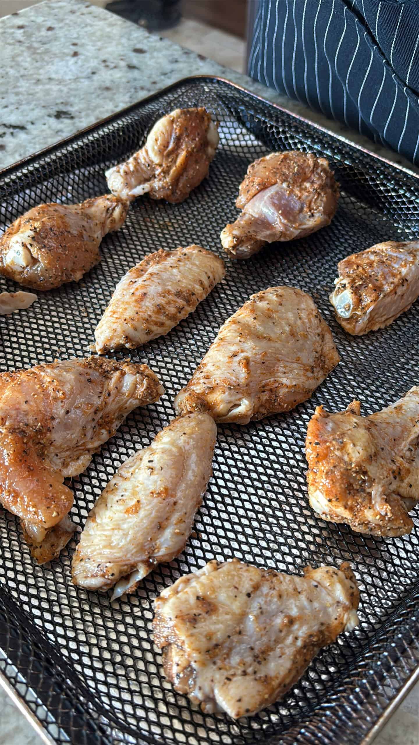Raw seasoned wings on a air fryer basket.