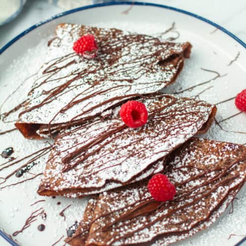 Chocolate Crepes dusted with powdered sugar and chocolate sauce.