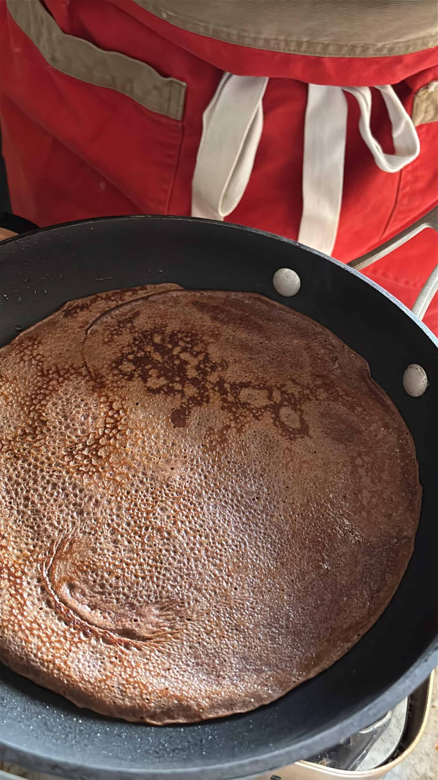 Chocolate crepes cooking in a skillet on second side.