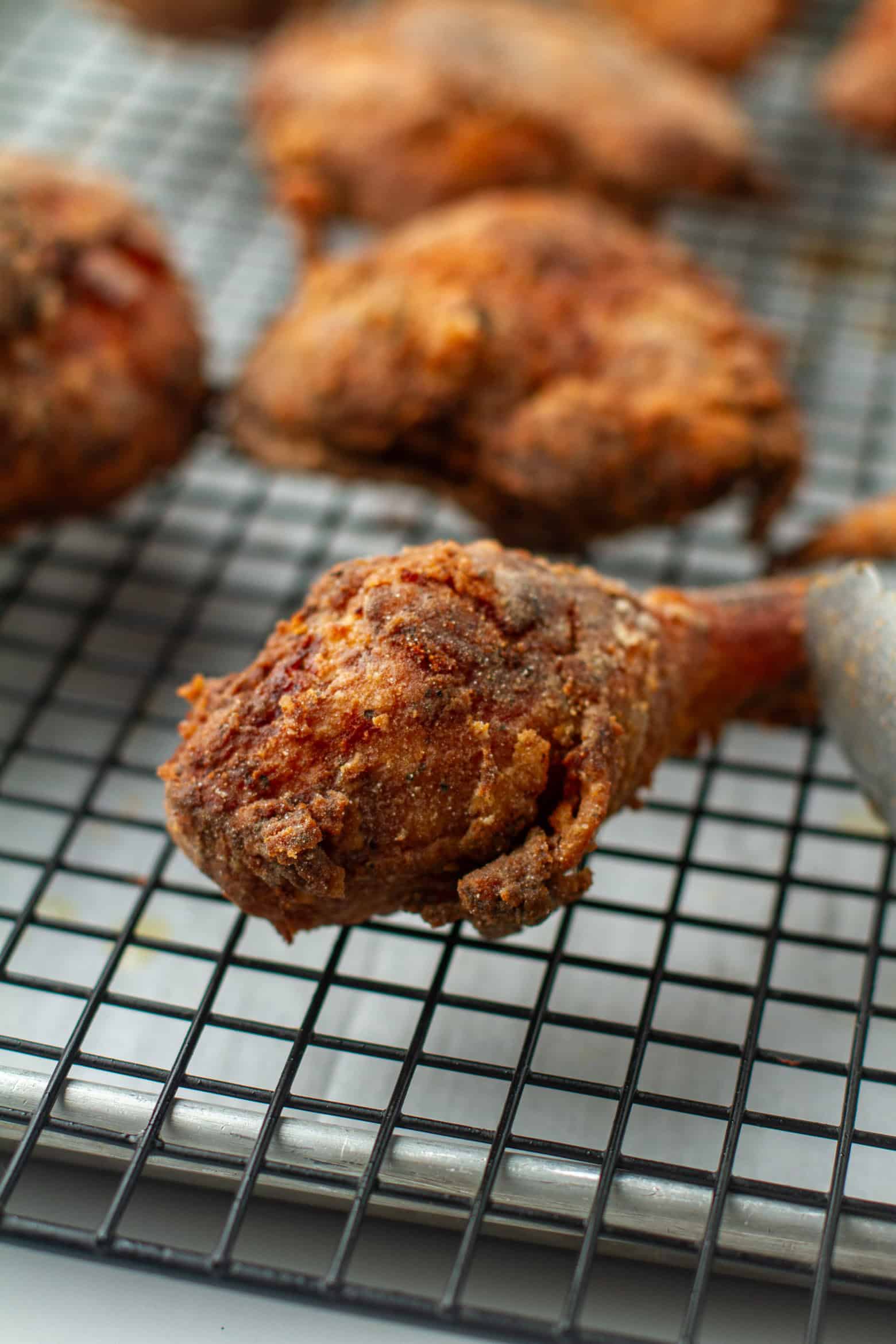Fried chicken leg cooling on a wired rack.