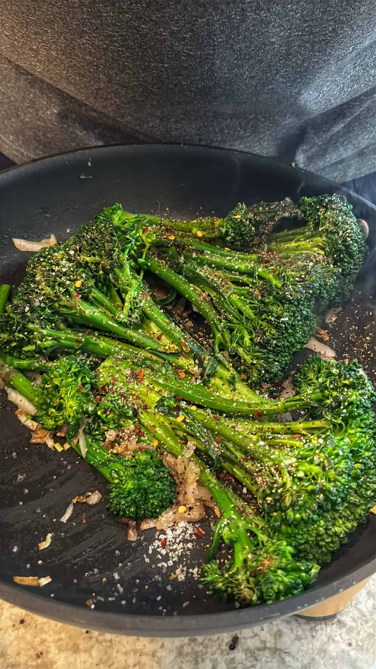 Seasonings added to broccolini cooking in a skillet.